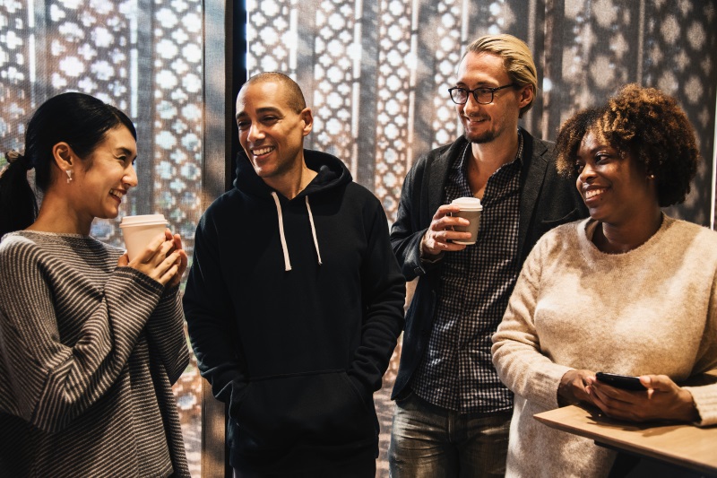 multi racial group of adults standing drinking coffee and chatting 