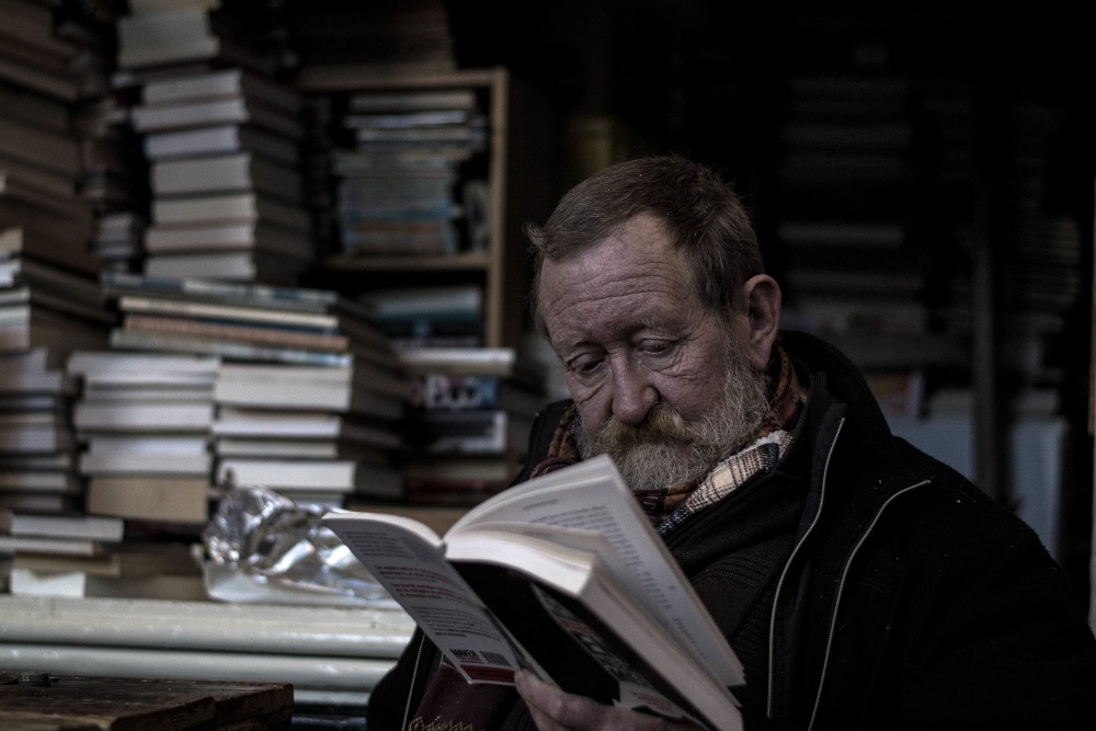 old man reading a book in a library